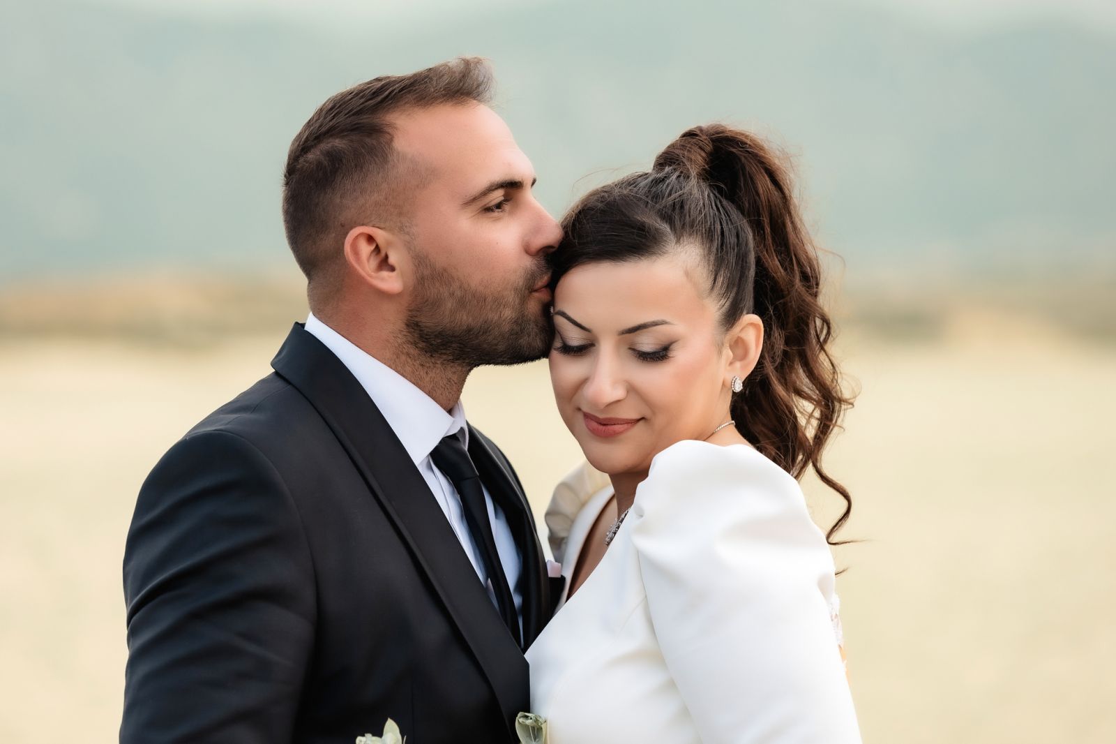 Groom kissing bride's forehead outdoors